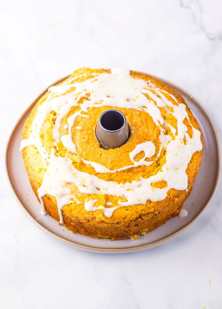 Round bundt cake with white glaze drizzled on top, displayed on a plate against a white marble background.