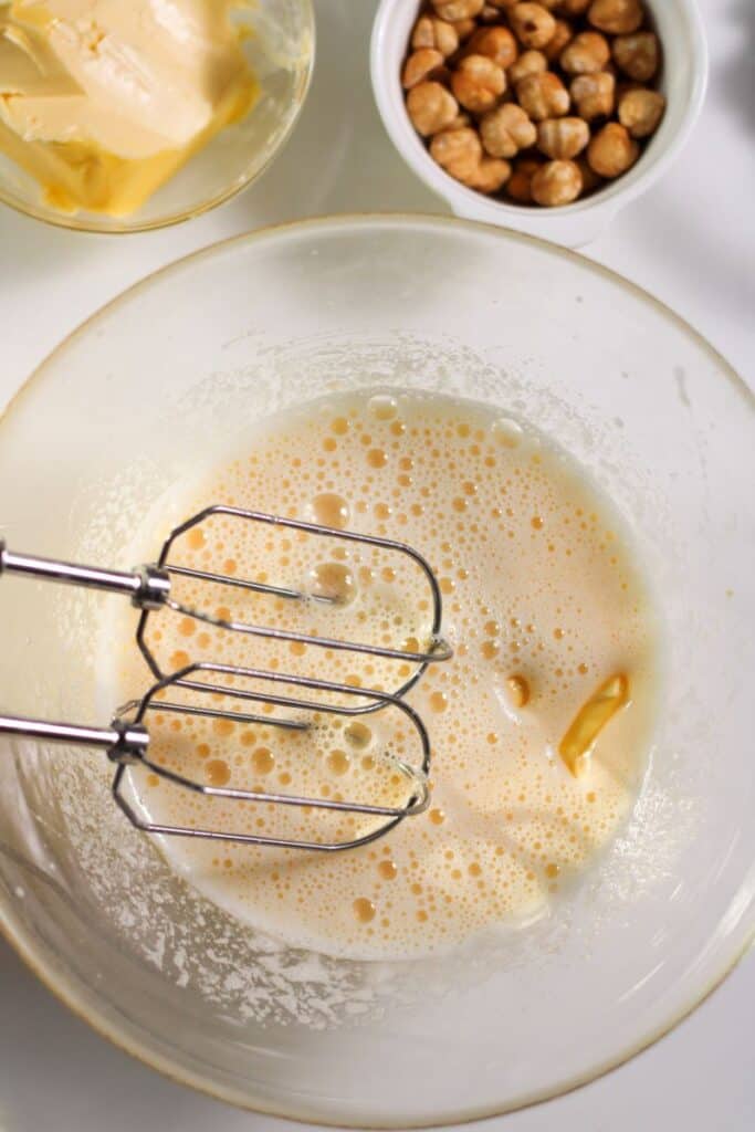 Overhead view of clear bowl with foamy liquid and mixer beaters.