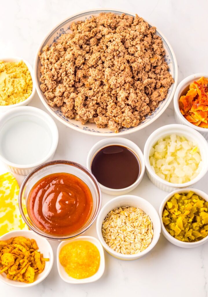Overhead view of ingredients for sloppy joes in white bowls on white background.
