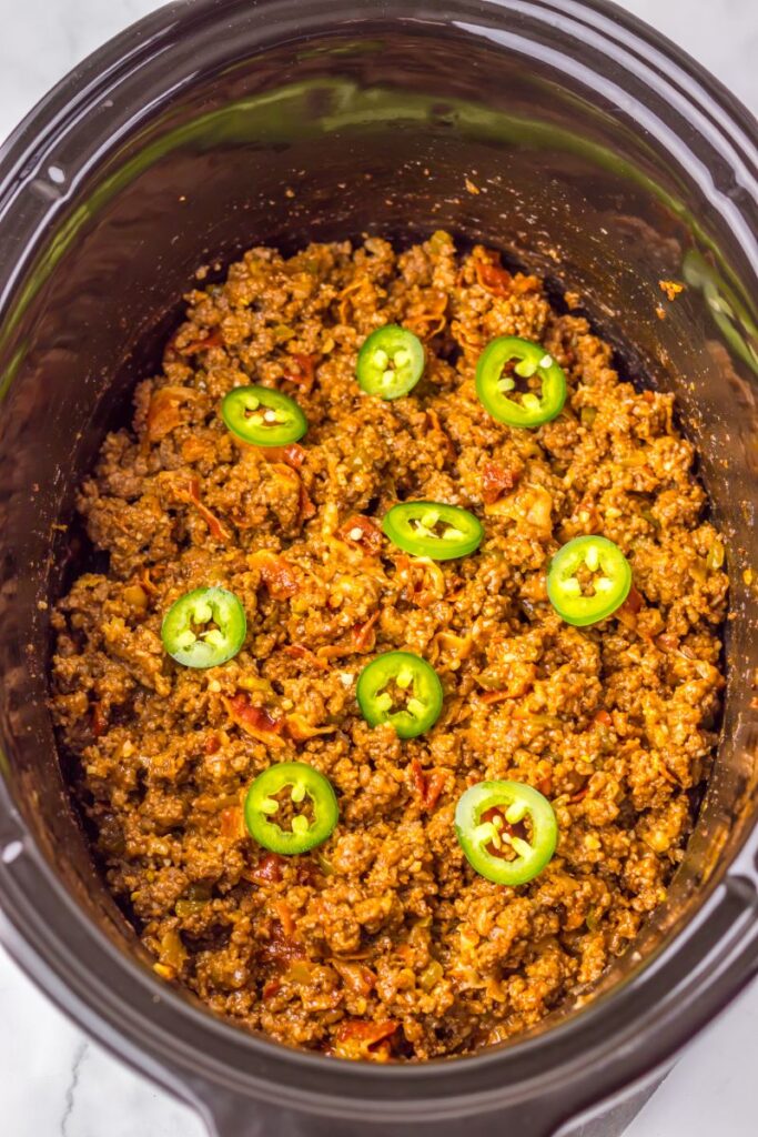 Overhead view of black crockpot with ground beef and sliced jalapenos.
