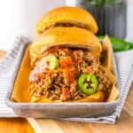 Side view of two hamburger buns filled with ground beef, bacon, and sliced jalapenos.