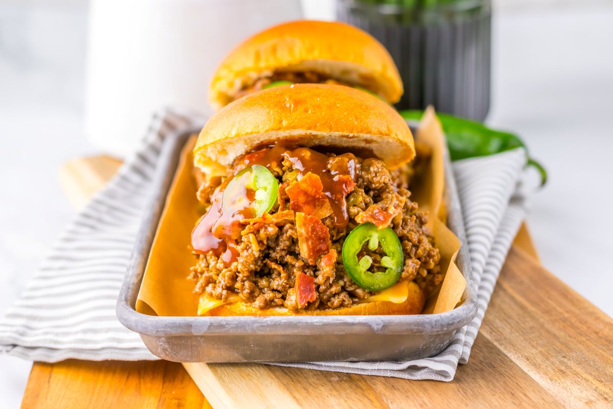 Side view of two hamburger buns filled with ground beef, bacon, and sliced jalapenos.