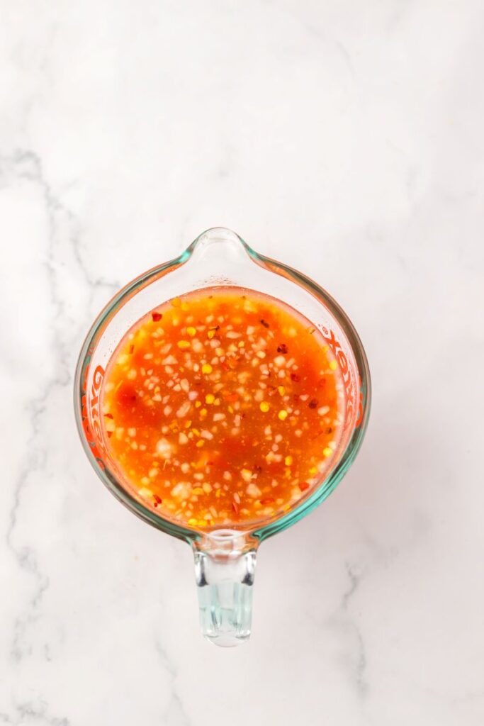 Overhead view of red sauce with specks in glass measuring cup.