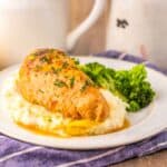 Side view of cooked chicken breast on mashed potatoes next to cooked broccoli on white plate.