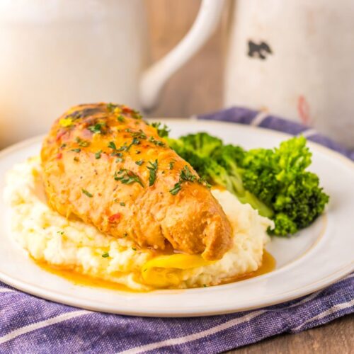 Side view of cooked chicken breast on mashed potatoes next to cooked broccoli on white plate.