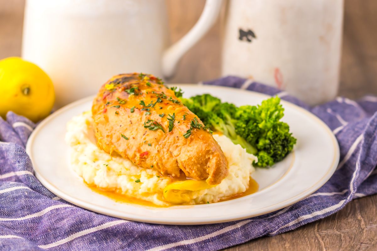 Side view of cooked chicken breast on mashed potatoes next to cooked broccoli on white plate.