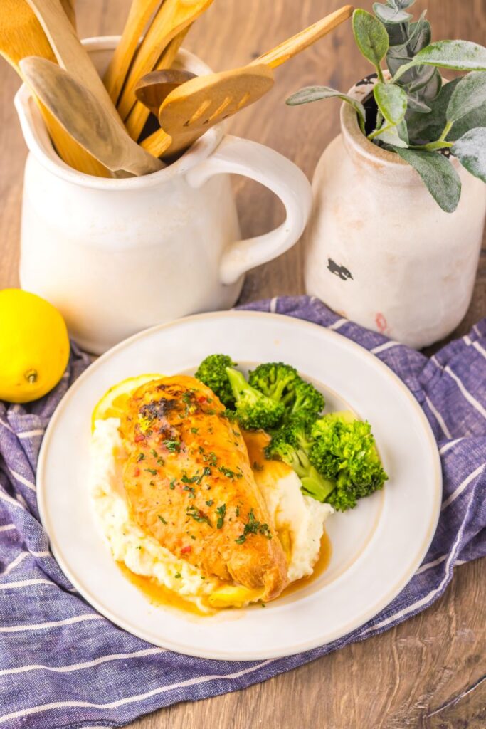 Overhead view of cooked chicken breast on mashed potatoes next to cooked broccoli on white plate.