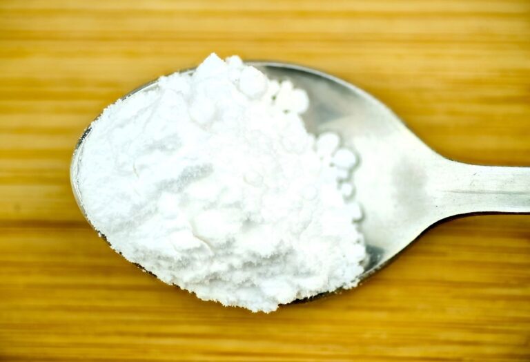 Close up of spoon with white powder on wooden background.
