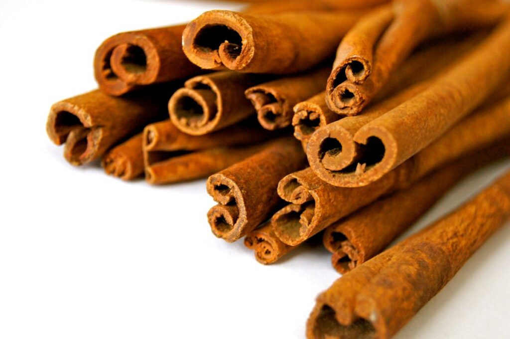 A close-up image of several cinnamon sticks lying on a white surface, showing their rolled, textured brown bark.