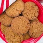A red plate filled with golden-brown, sugar-coated cookies, partially covered by a striped red, green, and white kitchen towel on a light-colored surface.