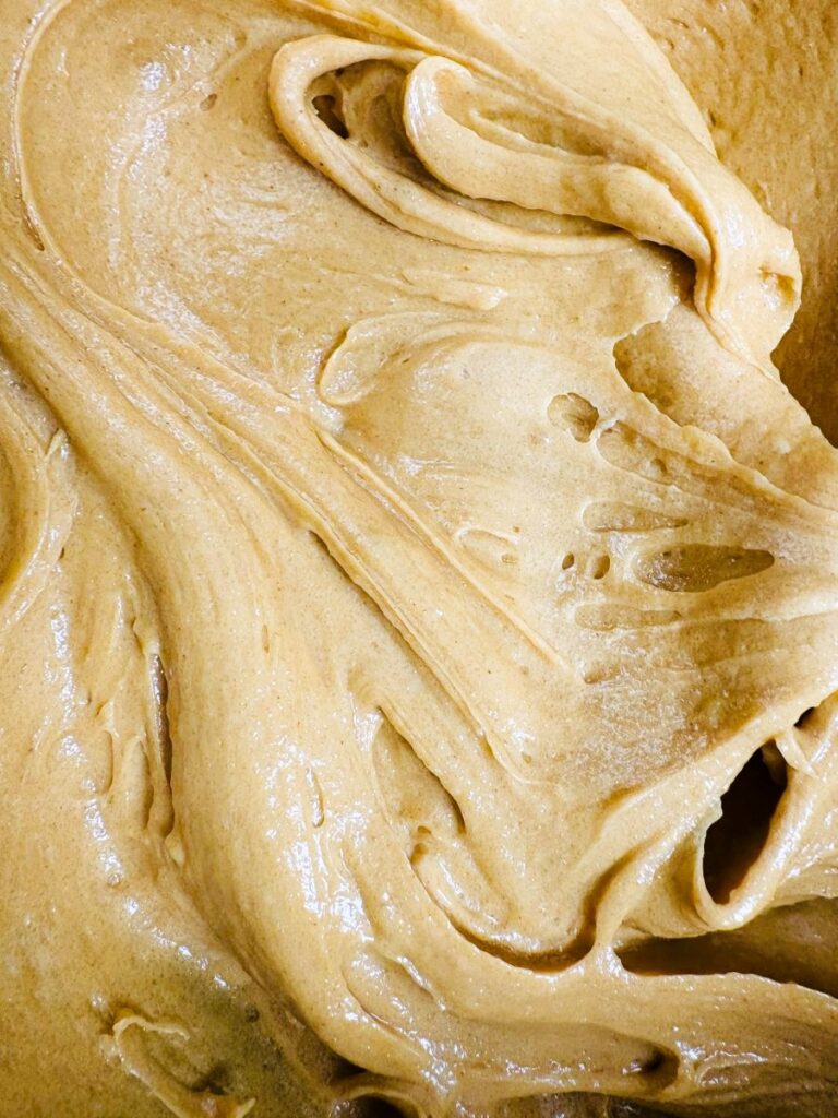 A close-up view of creamy, smooth peanut butter swirled in thick, glossy layers.