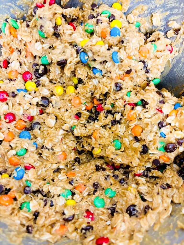 Close-up of cookie dough mixed with colorful candy-coated chocolates, chocolate chips, oats, and other ingredients, ready for baking.