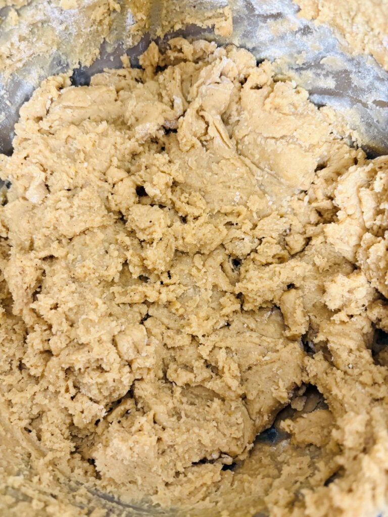 Close-up of a bowl filled with raw cookie dough, showing a thick, slightly crumbly texture with light brown color and uneven surface.