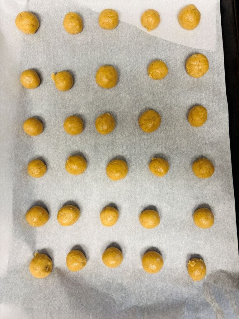 Thirty-five evenly spaced, round balls of cookie dough are arranged in a grid pattern on a parchment-lined baking sheet, ready for baking.