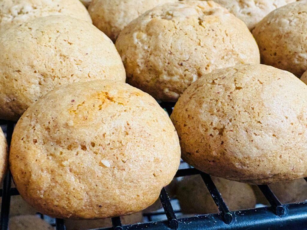 A close-up of several round, golden-brown cookies cooling on a metal rack. The cookies have a slightly cracked surface and look soft and freshly baked.