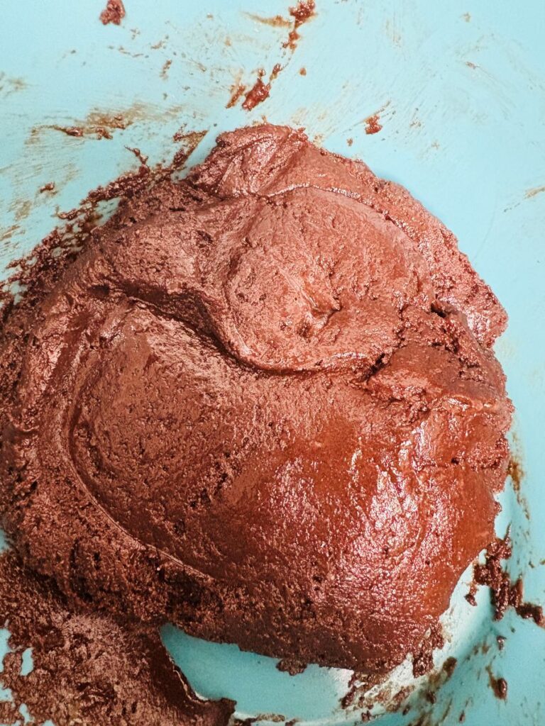 A close-up of thick, chocolate-colored dough or batter inside a light blue mixing bowl, with some smears of the mixture on the sides.