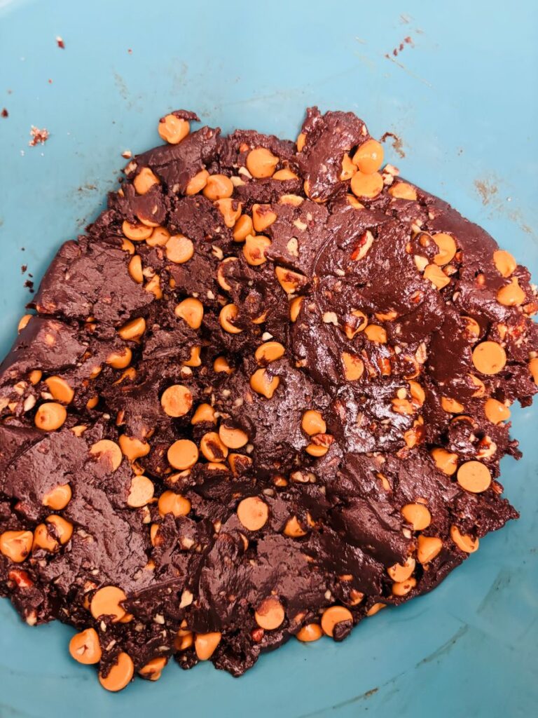 A close-up of chocolate cookie dough mixed with peanut butter chips in a blue mixing bowl.