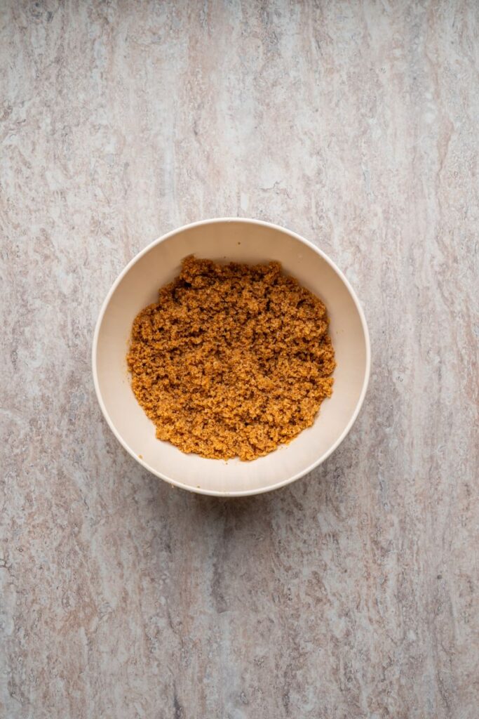 A white bowl filled with a crumbly brown mixture sits on a marbled light brown countertop.