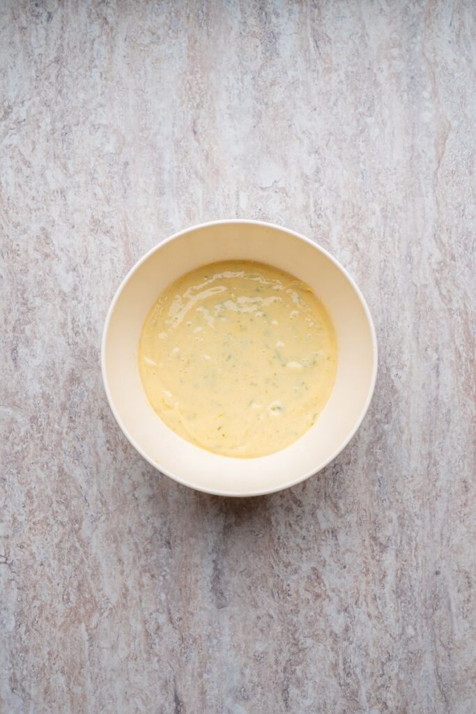 A white bowl filled with a creamy, pale yellow mixture sits on a light marbled countertop.