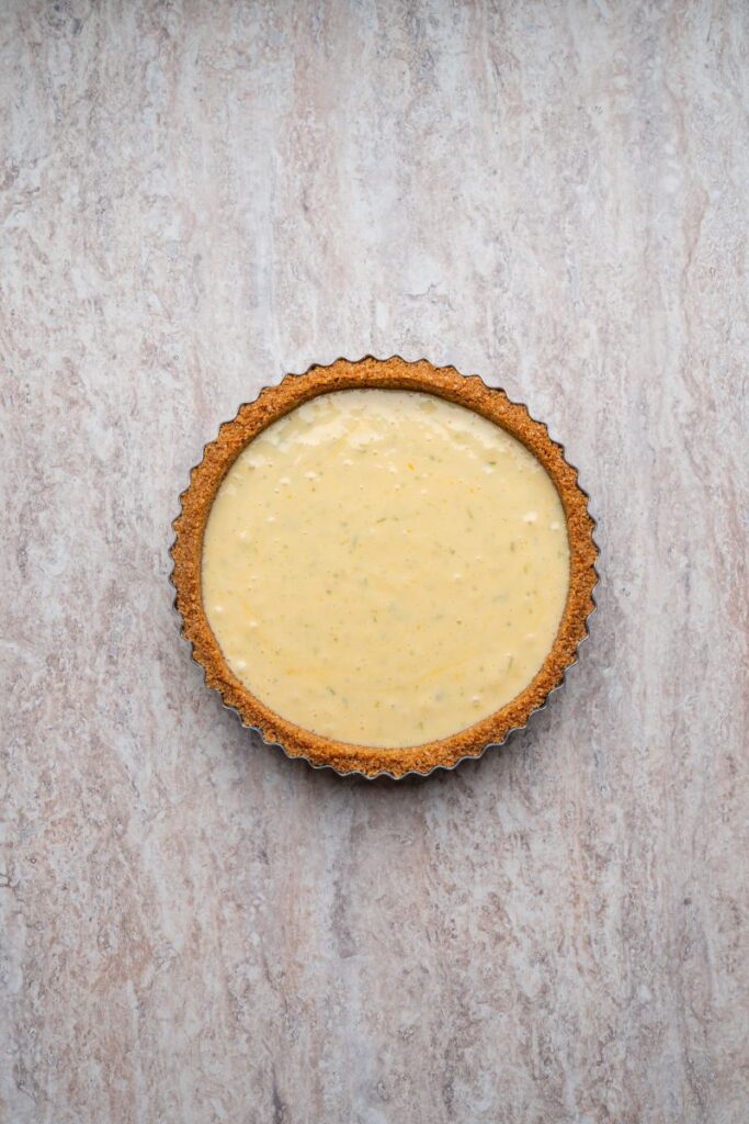 A round tart with a golden-brown crust and a creamy, pale yellow filling sits on a light marbled surface.
