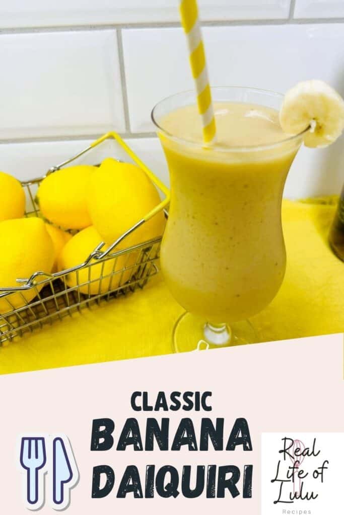 A glass of banana daiquiri with a yellow-striped straw and banana slice garnish sits on a yellow surface next to a basket of lemons. Text reads Classic Banana Daiquiri and Real Life of Lulu Recipes.