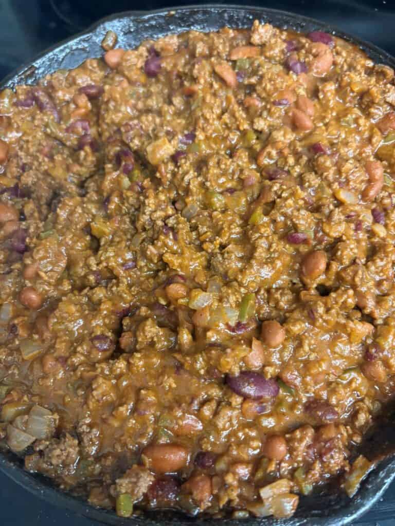A close-up of a skillet filled with homemade chili, featuring ground meat, kidney beans, pinto beans, onions, and a thick, rich sauce.