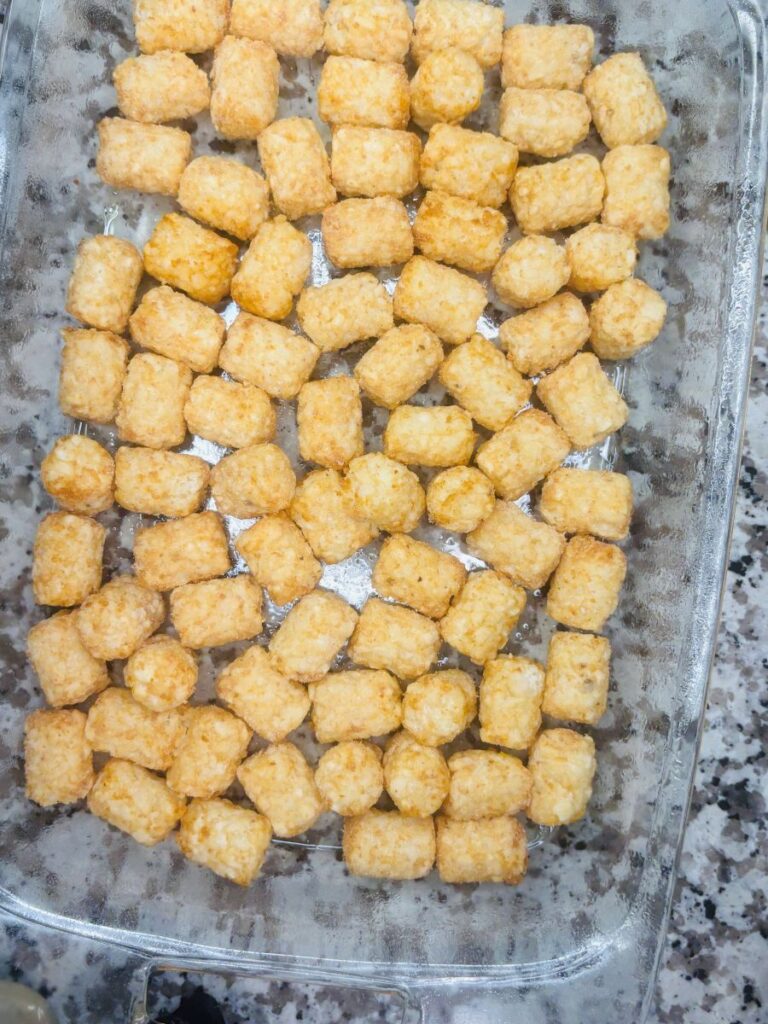 A glass baking dish filled with a single layer of golden brown tater tots, resting on a speckled countertop.