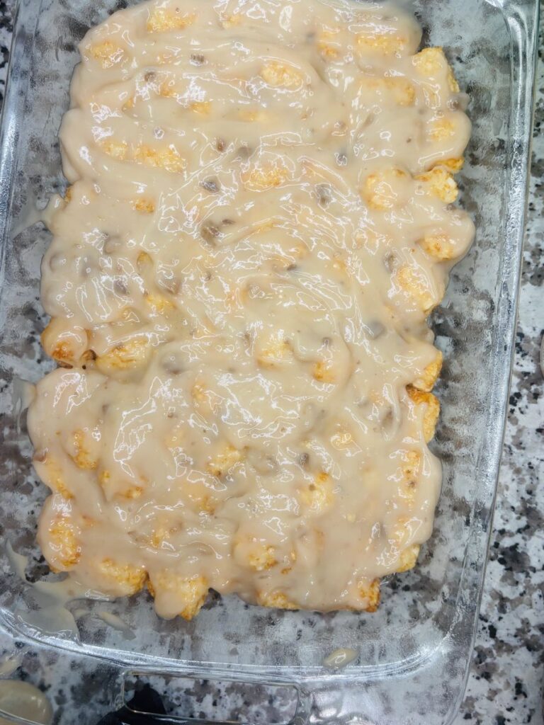 A glass baking dish filled with biscuit dough covered in a thick, creamy beige sauce, sitting on a granite countertop.