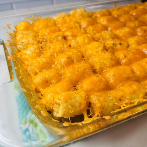 A glass casserole dish filled with golden tater tots topped with melted cheddar cheese, fresh from the oven, sitting on a kitchen counter.
