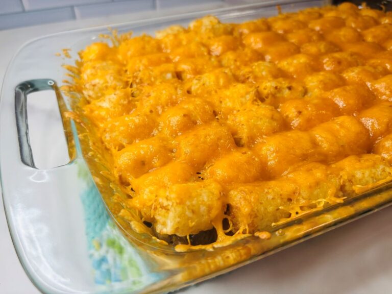 A glass casserole dish filled with golden tater tots topped with melted cheddar cheese, fresh from the oven, sitting on a kitchen counter.