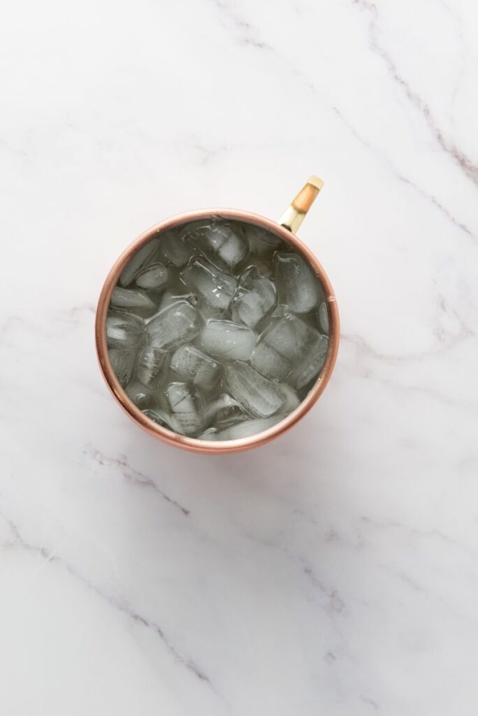 A copper mug filled with ice cubes sits on a white marble surface, viewed from above.