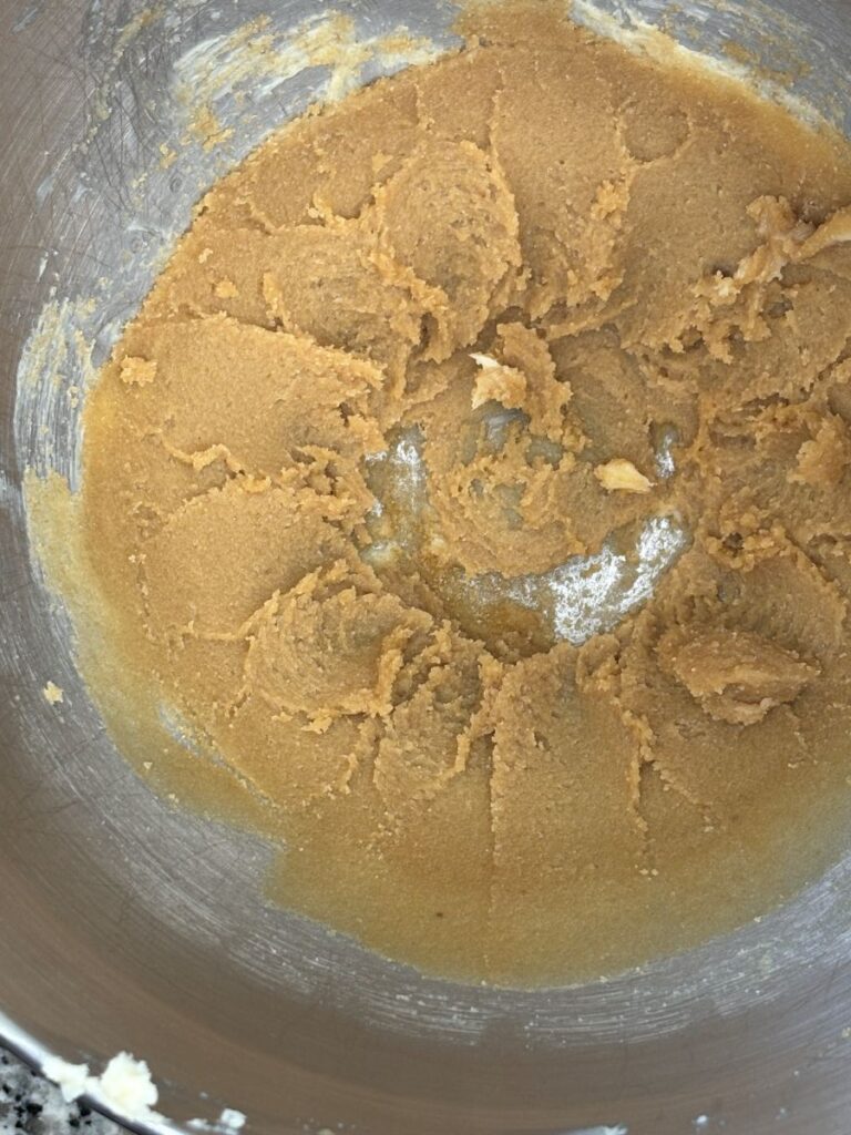 A mixing bowl containing light brown, creamy cookie dough with a ring of dough pressed around the sides and some dough clinging to the bowls surface.