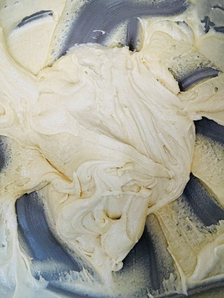 Thick, creamy cake batter being mixed in a metal bowl, with visible swirls and streaks from a mixing utensil.