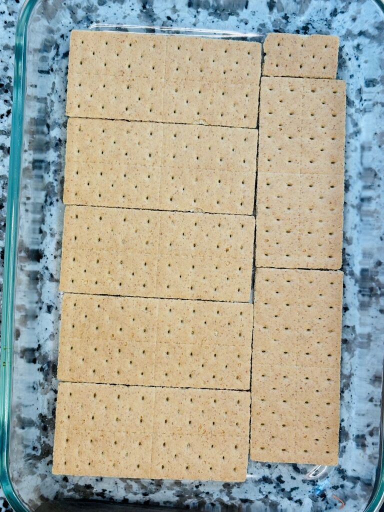 Rectangular graham crackers arranged in a single layer to fit the bottom of a glass baking dish, on a speckled countertop.