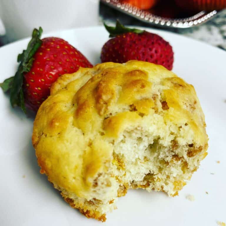 A close-up of a partially eaten muffin on a white plate, accompanied by two whole strawberries in the background.