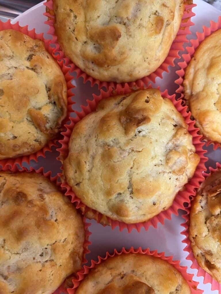A close-up view of several golden-brown muffins in red paper liners, arranged closely together on a white surface.
