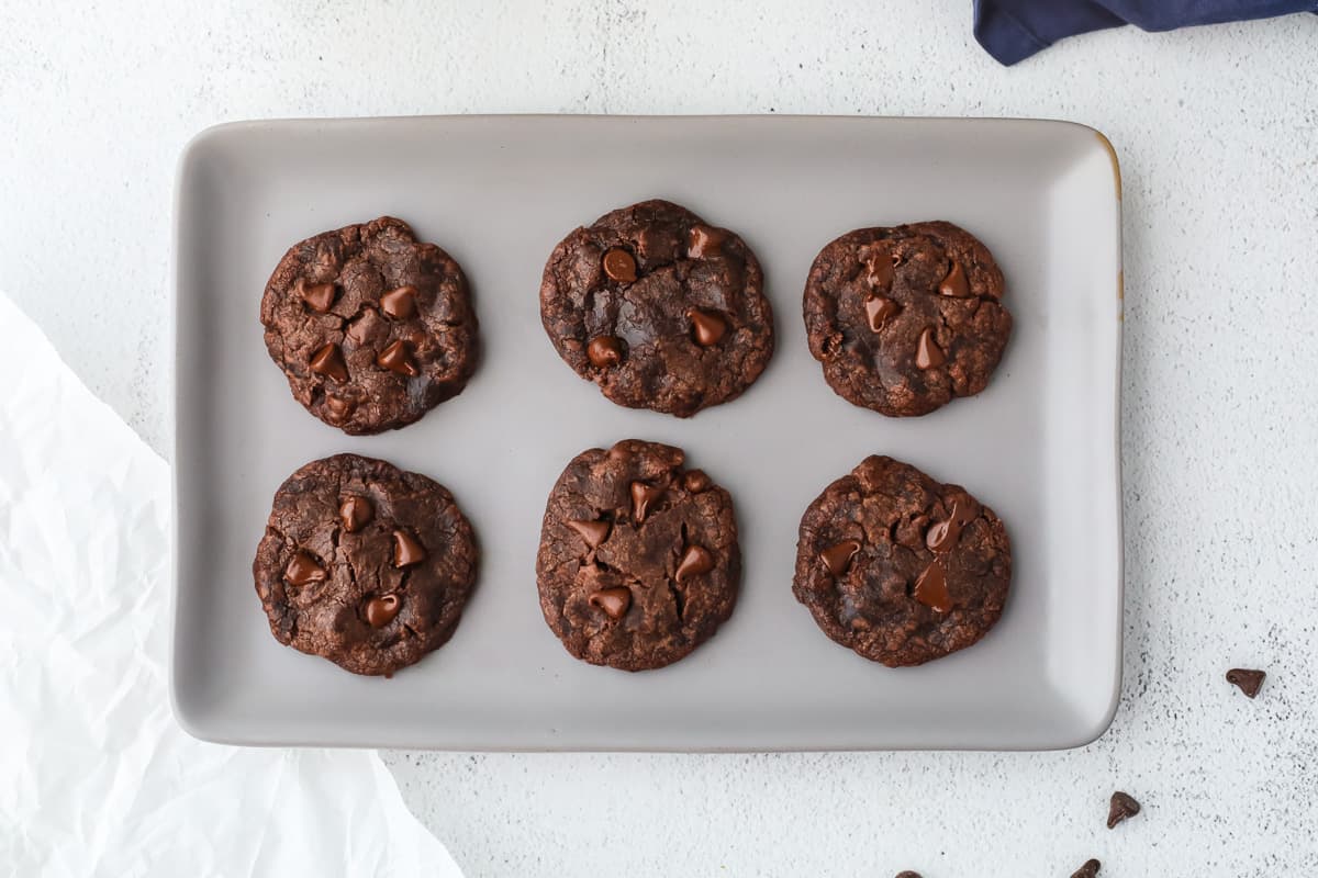 A rectangular gray plate with six chocolate cookies topped with chocolate chips, arranged in two rows of three, on a white surface.