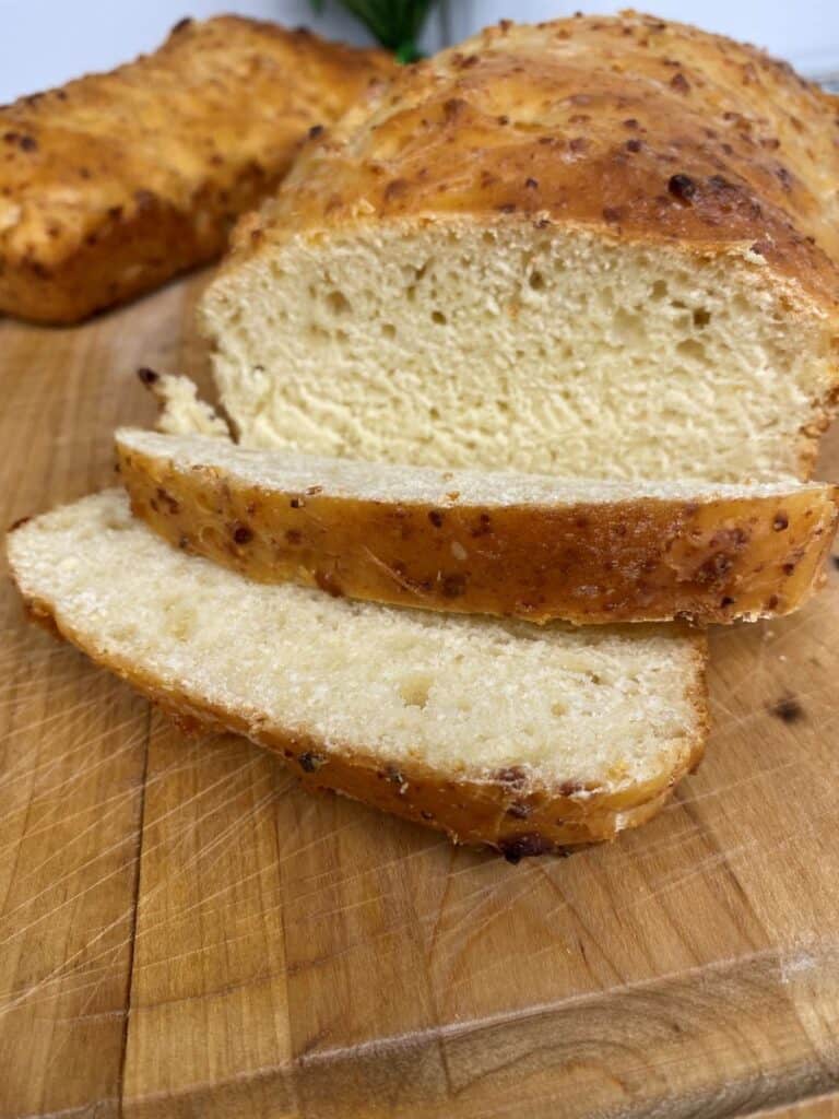 A loaf of golden-brown bread with a soft, airy interior sits on a wooden cutting board. Two slices have been cut from the loaf and are lying in front of it.