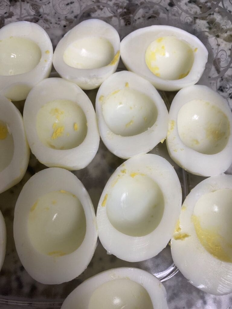 Several hard-boiled egg halves with the yolks removed are arranged in a close cluster, likely prepared for making deviled eggs. The egg whites are smooth with slight traces of yolk left inside.