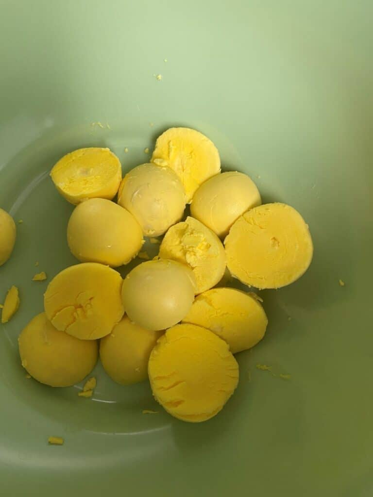 A group of hard-boiled egg yolks, some whole and some halved, sitting in a light green bowl.