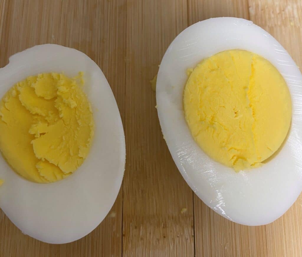 Two halves of a hard-boiled egg with firm, yellow yolks and white egg whites are placed on a wooden surface.