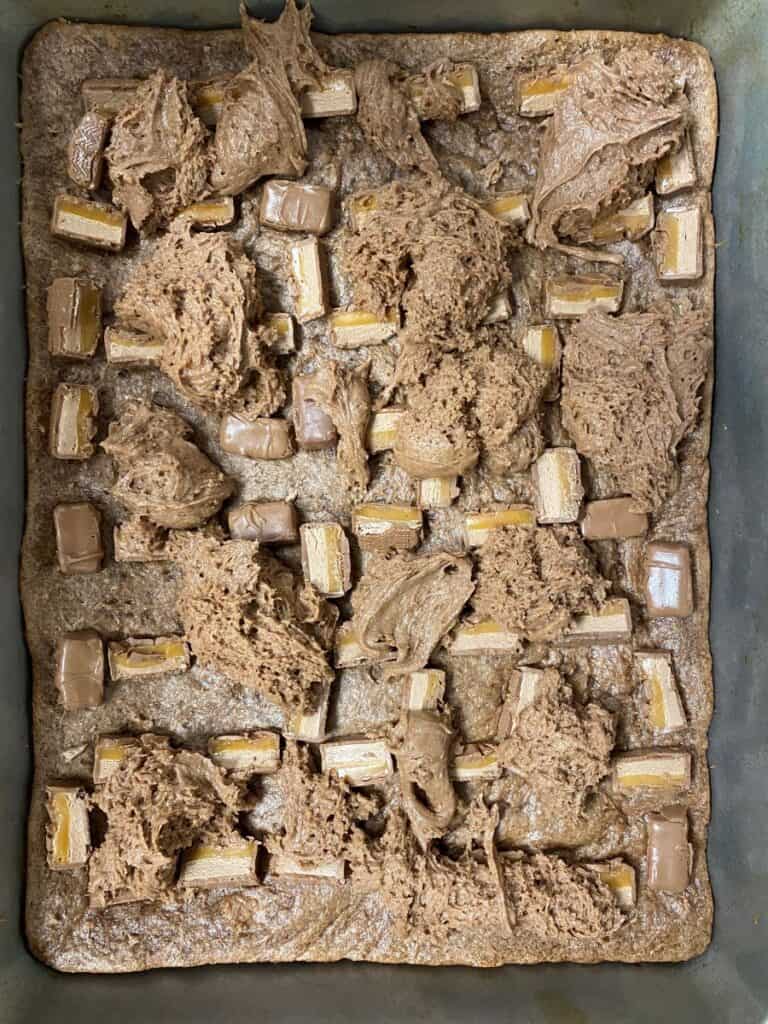 A baking pan filled with a chocolate batter, unevenly spread, and topped with pieces of chocolate-covered wafer bars placed in rows before baking.