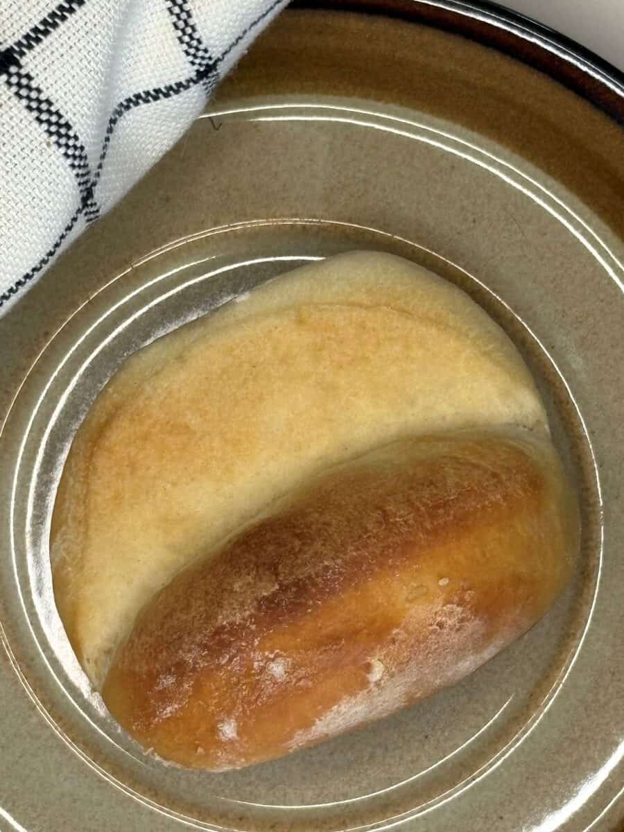 A round beige plate holds two pieces of bread, one lightly baked and pale, the other golden brown. A black-and-white checkered cloth is visible in the corner of the image.