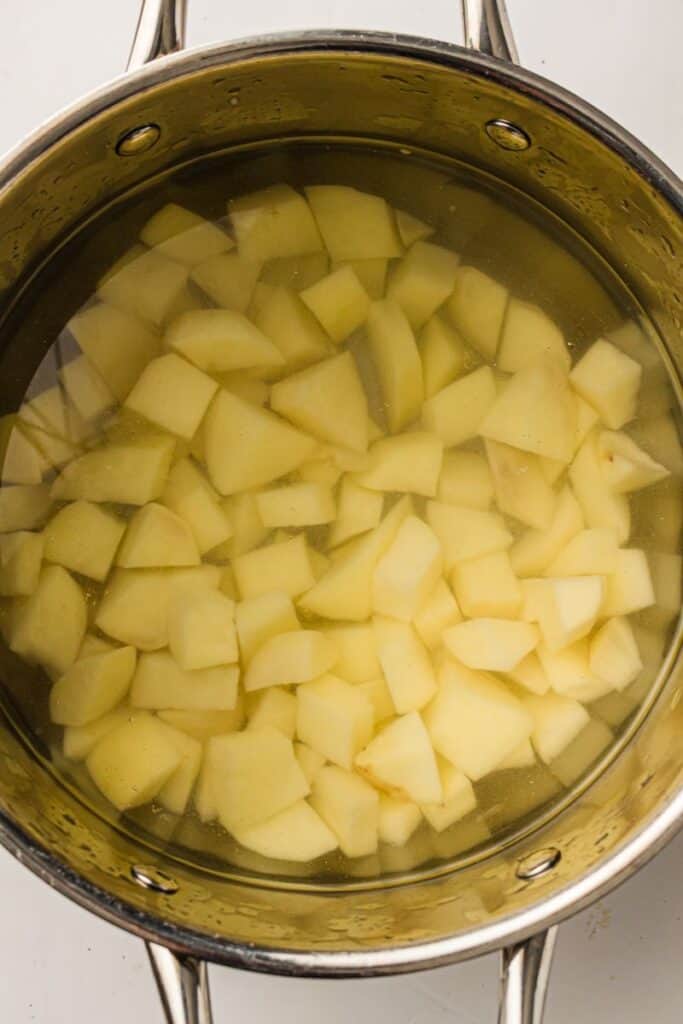 A stainless steel pot filled with water and chopped raw potatoes, ready to be cooked.