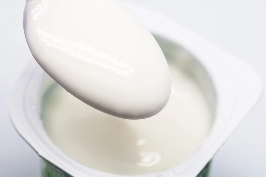 A close-up of a spoonful of plain white yogurt being lifted from an open yogurt container.