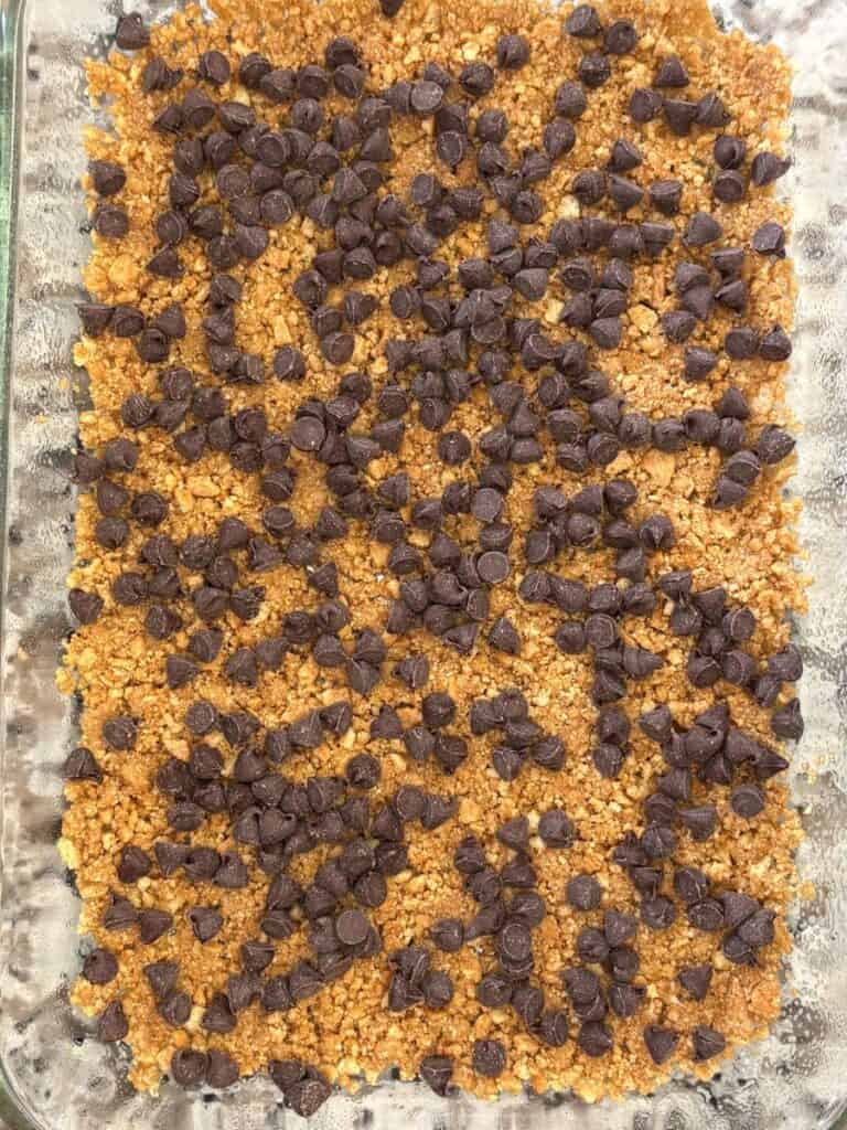 A glass baking dish filled with a crumbly golden-brown base, topped with a generous layer of scattered chocolate chips.