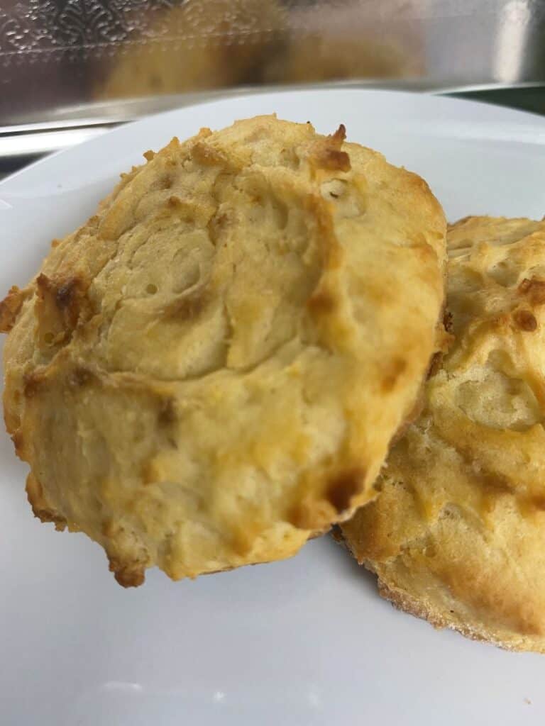 Two golden-brown biscuits with a slightly crisp, textured surface are placed on a white plate. The biscuits have a homemade, rustic appearance.