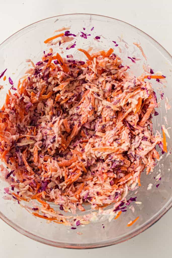 A glass bowl filled with creamy coleslaw made of shredded red cabbage, carrots, and white cabbage, all mixed with a mayonnaise-based dressing.