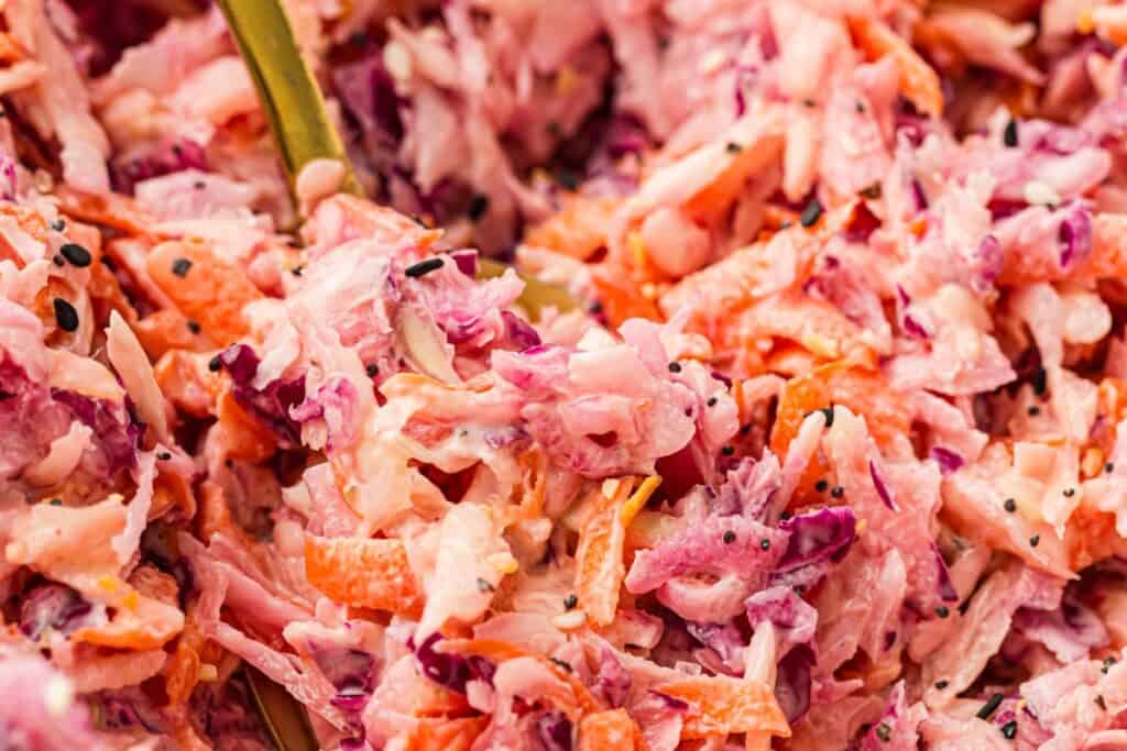 Close-up of creamy coleslaw featuring shredded red cabbage, carrots, and a creamy dressing, with a gold spoon partially visible in the mix.
