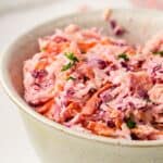 A close-up of a bowl filled with creamy coleslaw, featuring shredded cabbage, carrots, and a sprinkle of fresh herbs on top.